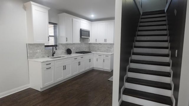 kitchen with a sink, stainless steel microwave, black gas cooktop, white cabinets, and dark wood-style flooring