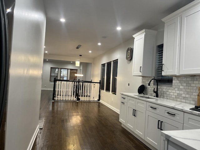 kitchen with a sink, backsplash, white cabinetry, light stone countertops, and dark wood-style flooring