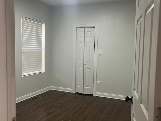 unfurnished bedroom featuring a closet, baseboards, visible vents, and dark wood-style flooring