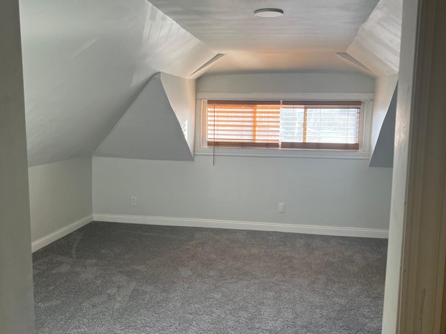 additional living space with baseboards, dark carpet, and vaulted ceiling