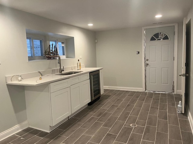 kitchen featuring a sink, baseboards, beverage cooler, and white cabinets