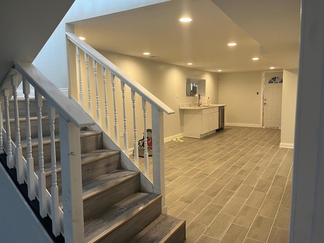 stairs featuring wood finished floors, beverage cooler, baseboards, wet bar, and recessed lighting