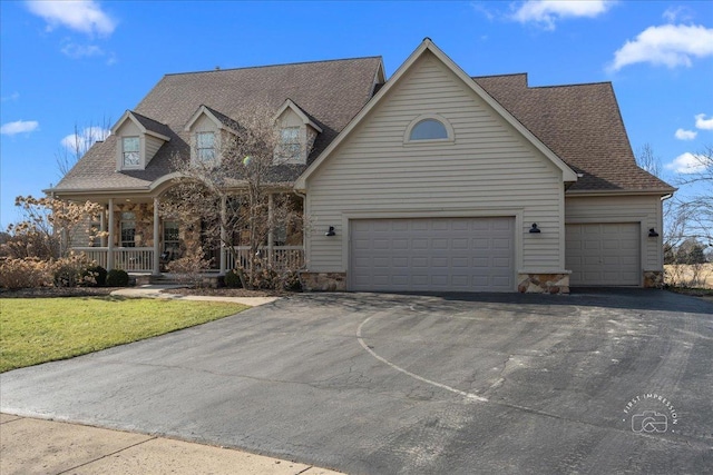 new england style home with a shingled roof, a front lawn, aphalt driveway, a porch, and stone siding