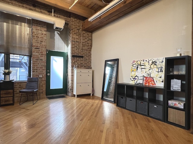 interior space featuring beamed ceiling, brick wall, wood finished floors, and a towering ceiling