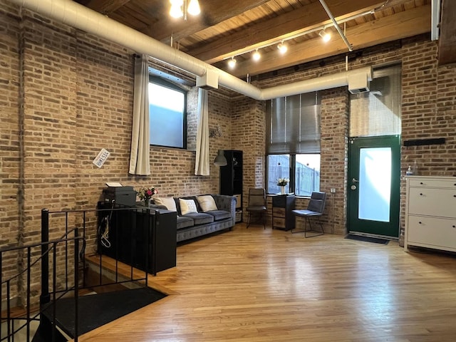 unfurnished living room featuring track lighting, brick wall, wood ceiling, a towering ceiling, and wood finished floors