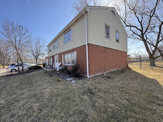 view of side of home featuring brick siding, a yard, and fence