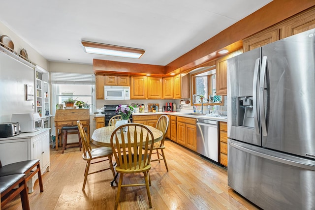 kitchen featuring light wood-type flooring, light countertops, brown cabinets, stainless steel appliances, and a sink