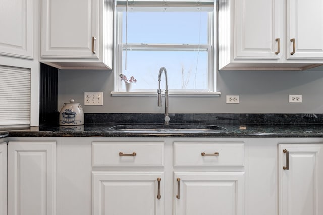 kitchen featuring dark stone countertops, white cabinetry, and a sink