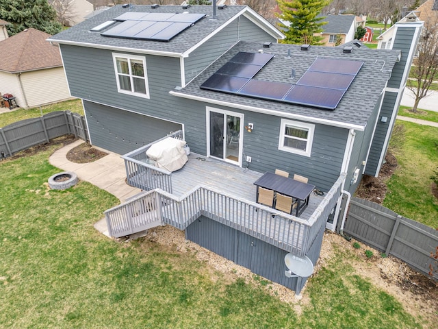 back of property featuring roof with shingles, a wooden deck, a fenced backyard, an outdoor fire pit, and a lawn