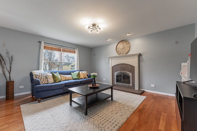 living room featuring baseboards, a tiled fireplace, and hardwood / wood-style flooring