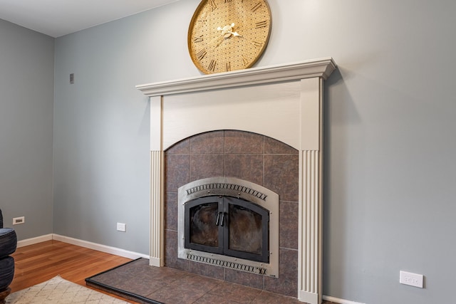 interior details with a tiled fireplace, baseboards, and wood finished floors