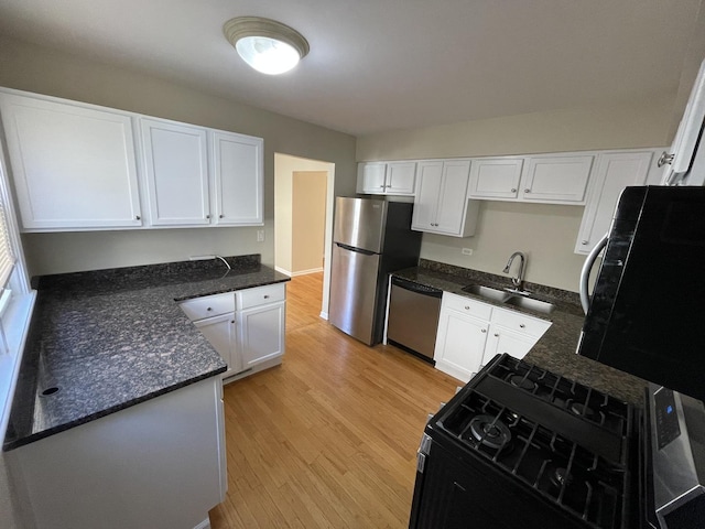 kitchen featuring appliances with stainless steel finishes, white cabinetry, light wood-style floors, and a sink