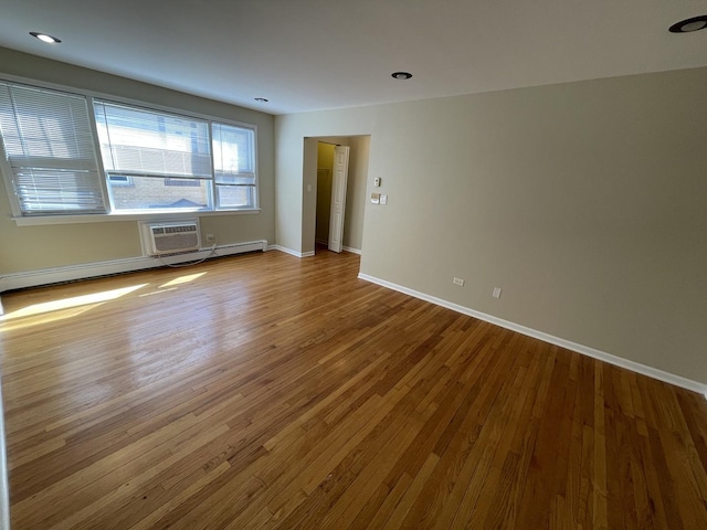 spare room featuring baseboard heating, a wall mounted air conditioner, baseboards, and wood finished floors