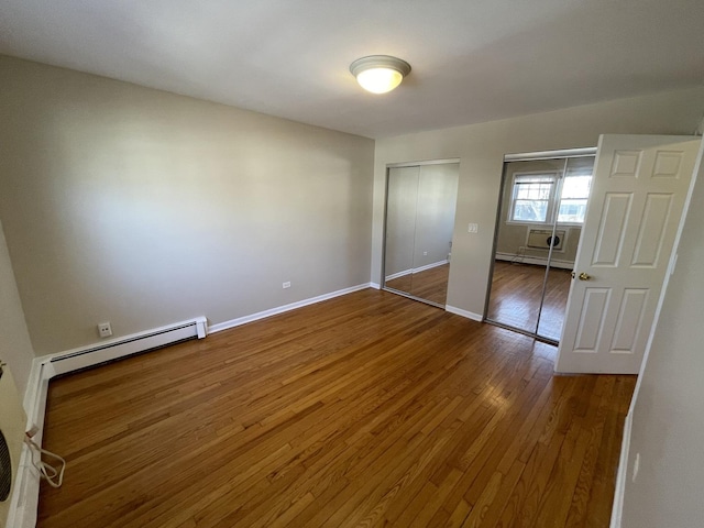 unfurnished bedroom with baseboard heating, baseboards, multiple closets, and wood-type flooring