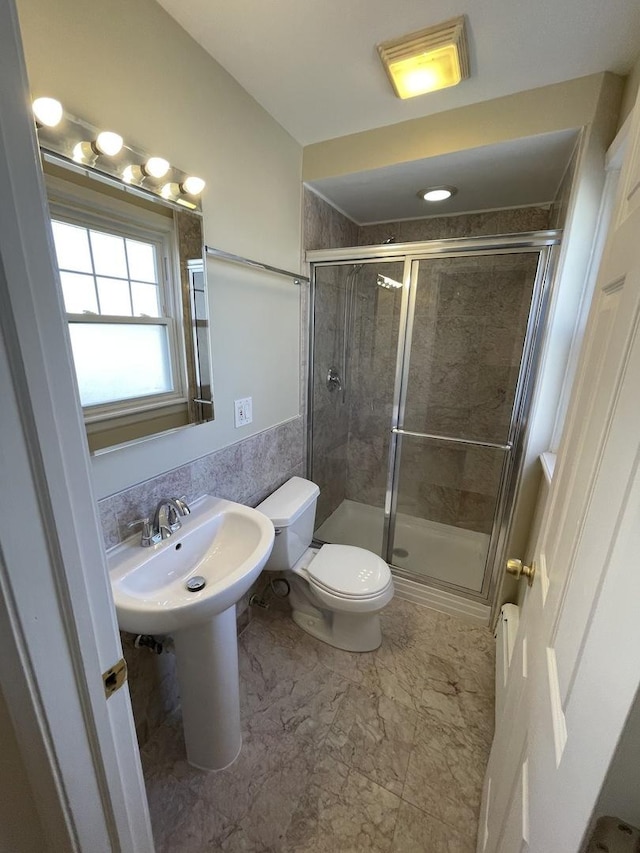 full bathroom with a wainscoted wall, toilet, a stall shower, a sink, and tile walls