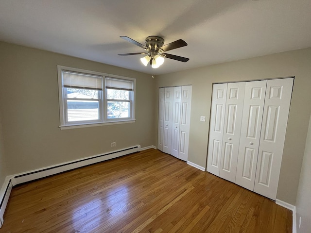 unfurnished bedroom with multiple closets, wood finished floors, baseboards, baseboard heating, and ceiling fan