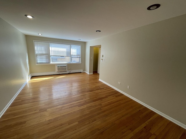 empty room with wood finished floors, baseboards, recessed lighting, a wall mounted air conditioner, and a baseboard heating unit