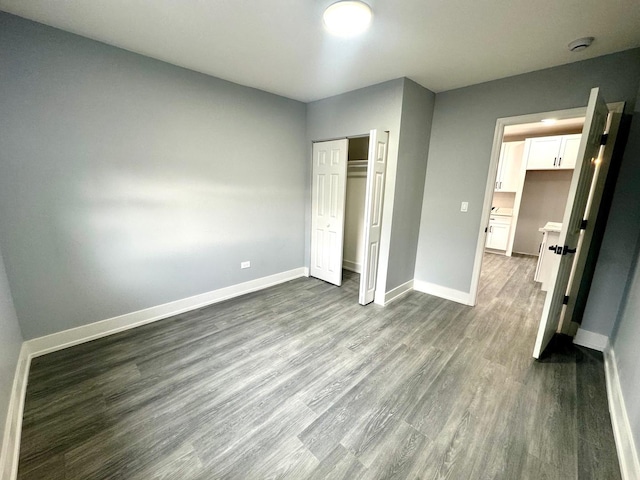 unfurnished bedroom with dark wood-style floors, a closet, and baseboards