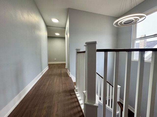 corridor with an upstairs landing, a chandelier, baseboards, and wood finished floors