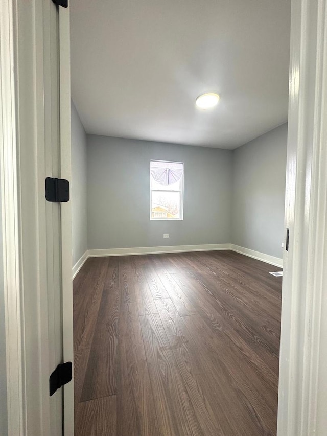 unfurnished room featuring baseboards and dark wood-style floors