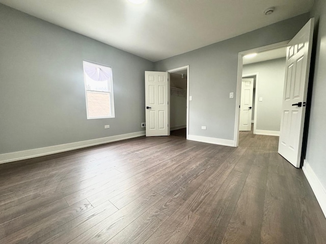 unfurnished bedroom featuring a walk in closet, baseboards, and dark wood-type flooring