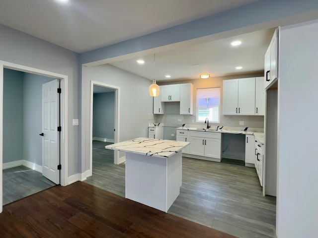 kitchen with dark wood-style floors, a center island, baseboards, and a sink