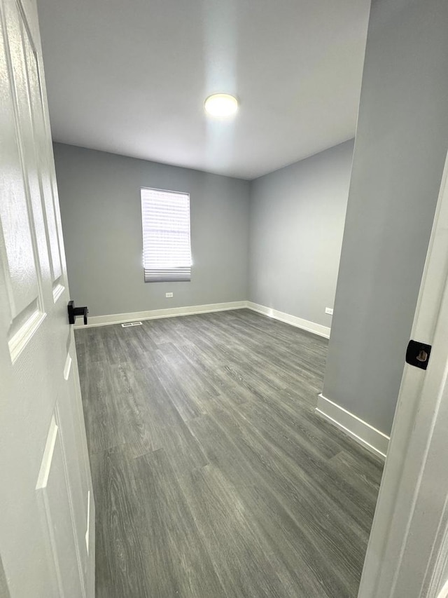 unfurnished room with dark wood finished floors, visible vents, and baseboards