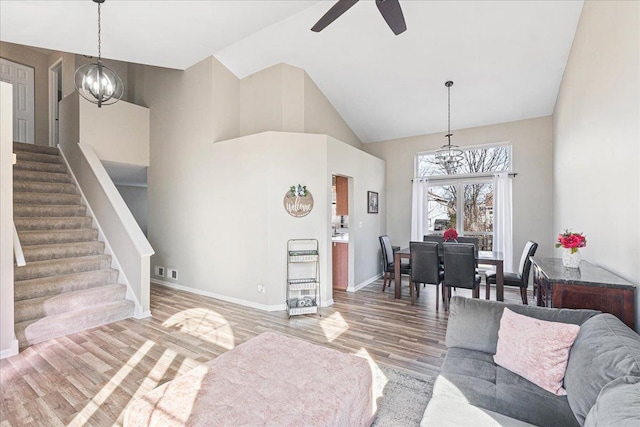 living room with high vaulted ceiling, ceiling fan with notable chandelier, wood finished floors, stairway, and baseboards