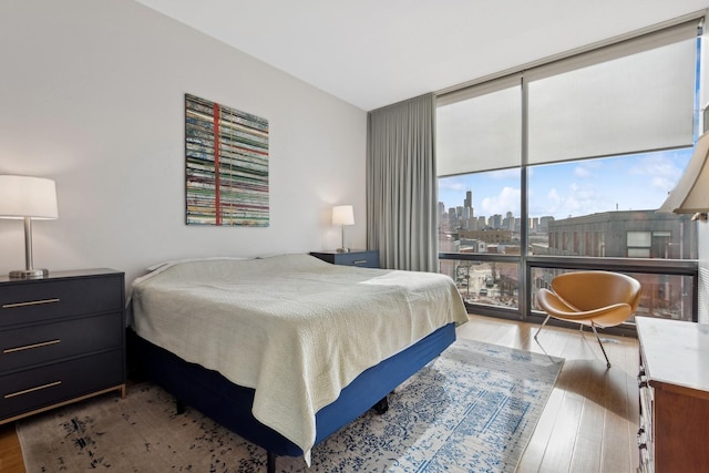 bedroom with a wall of windows, a city view, and wood finished floors