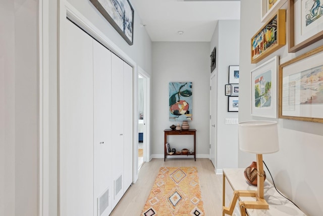 hall featuring light wood-type flooring, baseboards, and visible vents