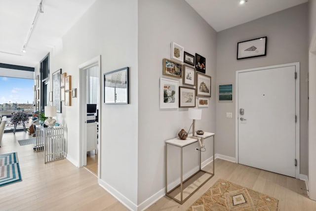 entrance foyer featuring floor to ceiling windows, light wood-style flooring, rail lighting, and baseboards