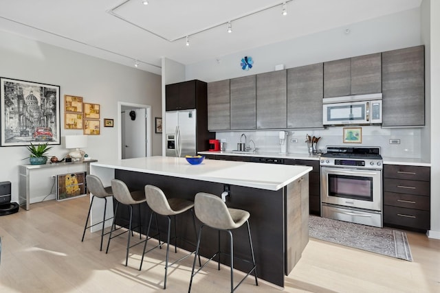 kitchen featuring tasteful backsplash, a breakfast bar area, light wood-type flooring, light countertops, and appliances with stainless steel finishes