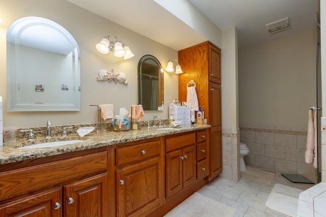 full bath with a sink, toilet, tile walls, and double vanity