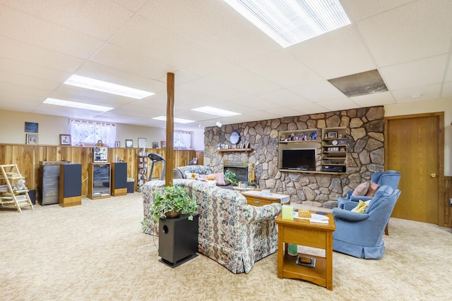 carpeted living room with a stone fireplace, a paneled ceiling, wooden walls, and a wainscoted wall
