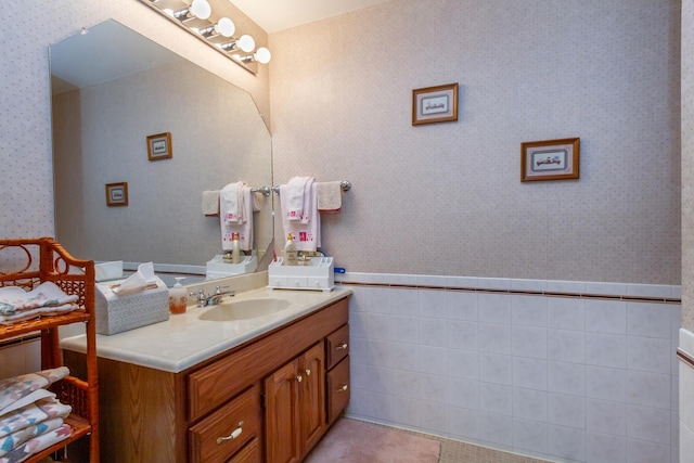 bathroom featuring tile walls, wainscoting, wallpapered walls, and vanity