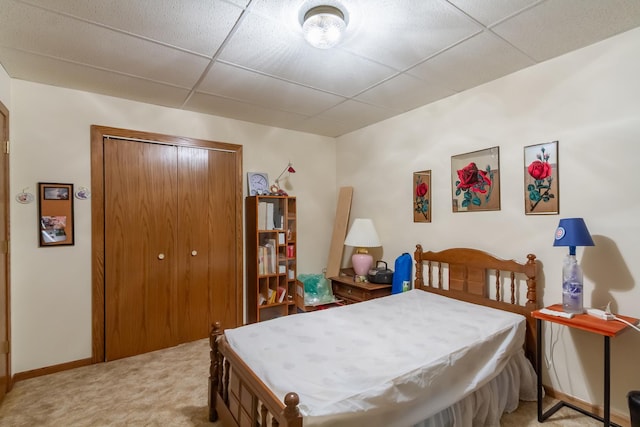bedroom featuring baseboards, a closet, a drop ceiling, and light carpet