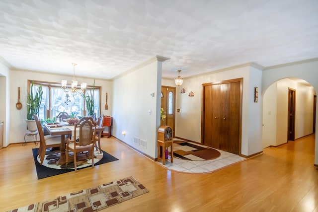 dining space with arched walkways, visible vents, light wood-style flooring, and a chandelier