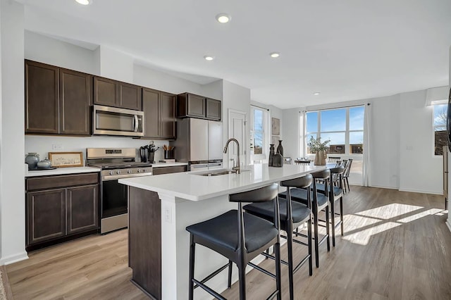 kitchen with a kitchen island with sink, light countertops, a kitchen breakfast bar, stainless steel appliances, and a sink