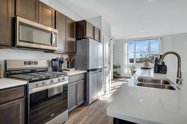 kitchen with dark brown cabinetry, vaulted ceiling, light wood-style floors, stainless steel appliances, and a sink