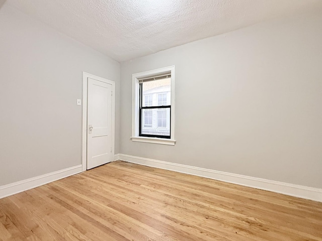 unfurnished room featuring light wood-style floors, baseboards, and a textured ceiling