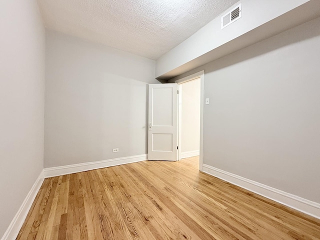 empty room with visible vents, light wood-style flooring, a textured ceiling, and baseboards