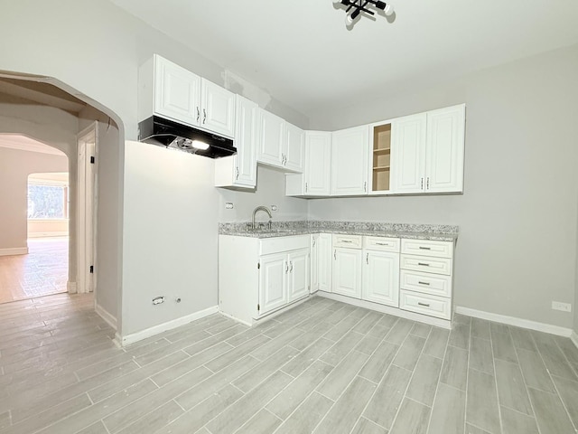 kitchen featuring a sink, arched walkways, light wood-style floors, and white cabinets