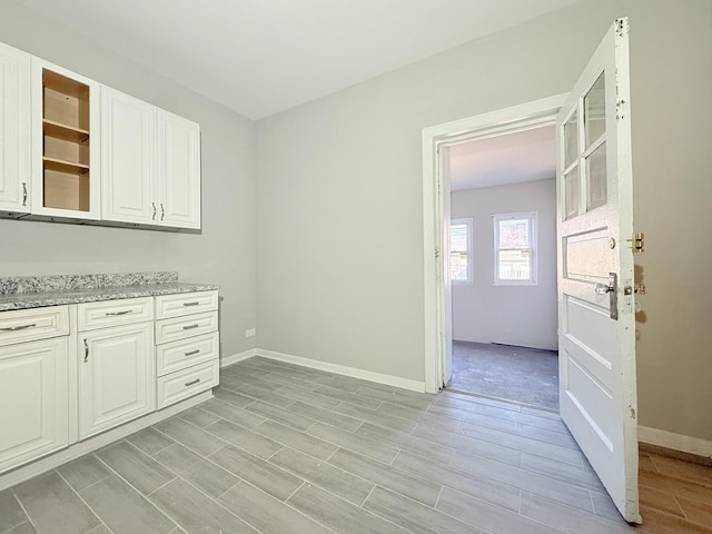 interior space with glass insert cabinets, baseboards, light stone countertops, white cabinets, and open shelves