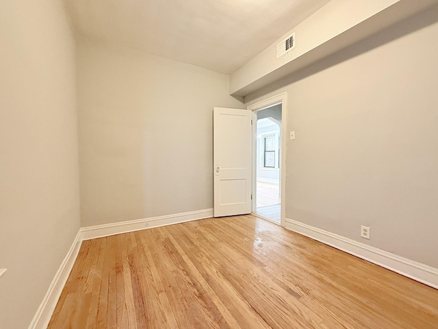 empty room with light wood finished floors, visible vents, and baseboards