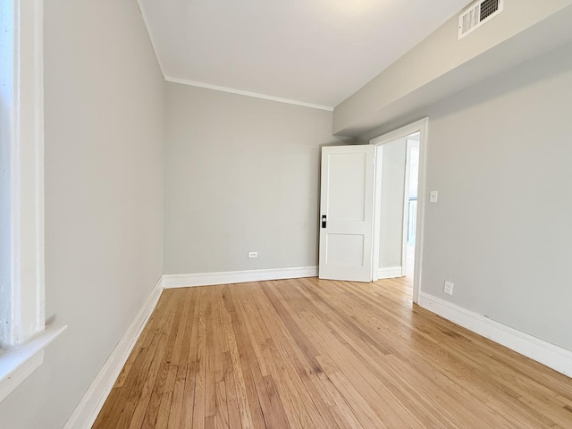 spare room with light wood-type flooring, baseboards, visible vents, and ornamental molding