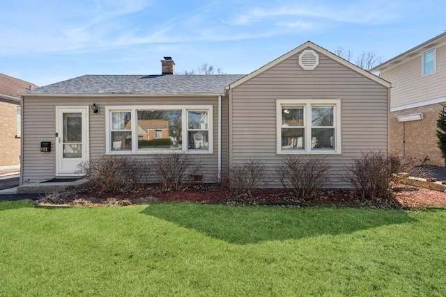 view of front of home with roof with shingles, a chimney, and a front lawn