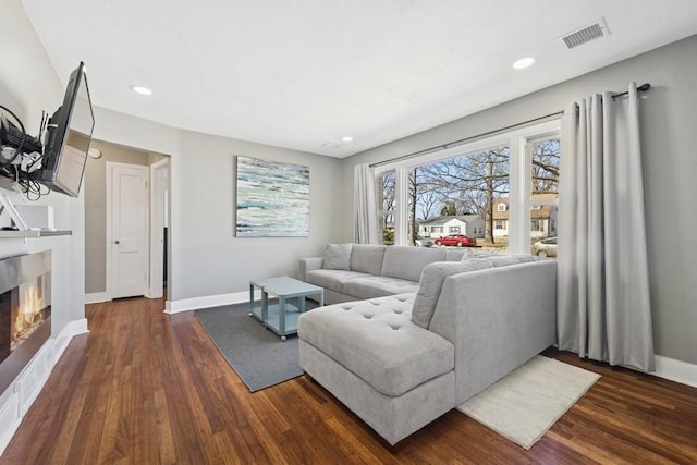 living area featuring visible vents, baseboards, recessed lighting, wood finished floors, and a glass covered fireplace