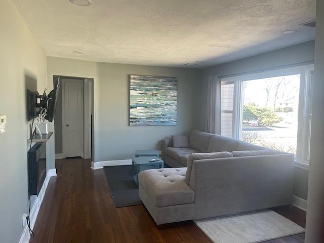 living room featuring a textured ceiling, dark wood-type flooring, and baseboards