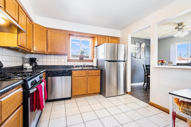 kitchen with tasteful backsplash, under cabinet range hood, brown cabinets, appliances with stainless steel finishes, and a sink