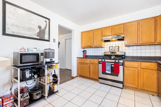 kitchen with dark countertops, under cabinet range hood, decorative backsplash, brown cabinetry, and stainless steel appliances